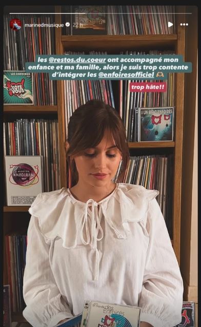 La chanteuse Marine assise devant une bibliothèque remplie de CD des Enfoirés.